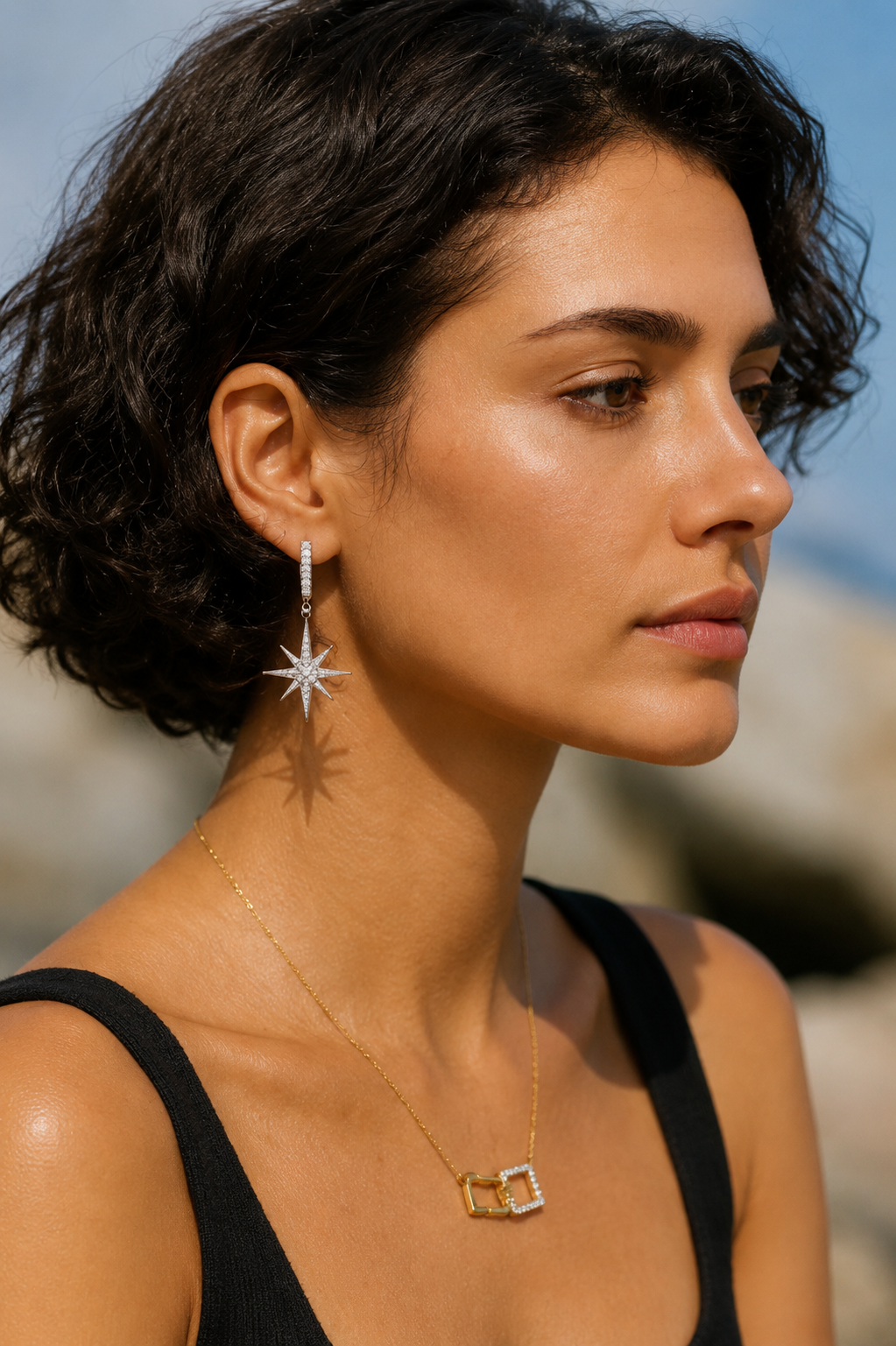 Side profile of a woman wearing North Star drop earrings and a geometric gold necklace in natural outdoor light.