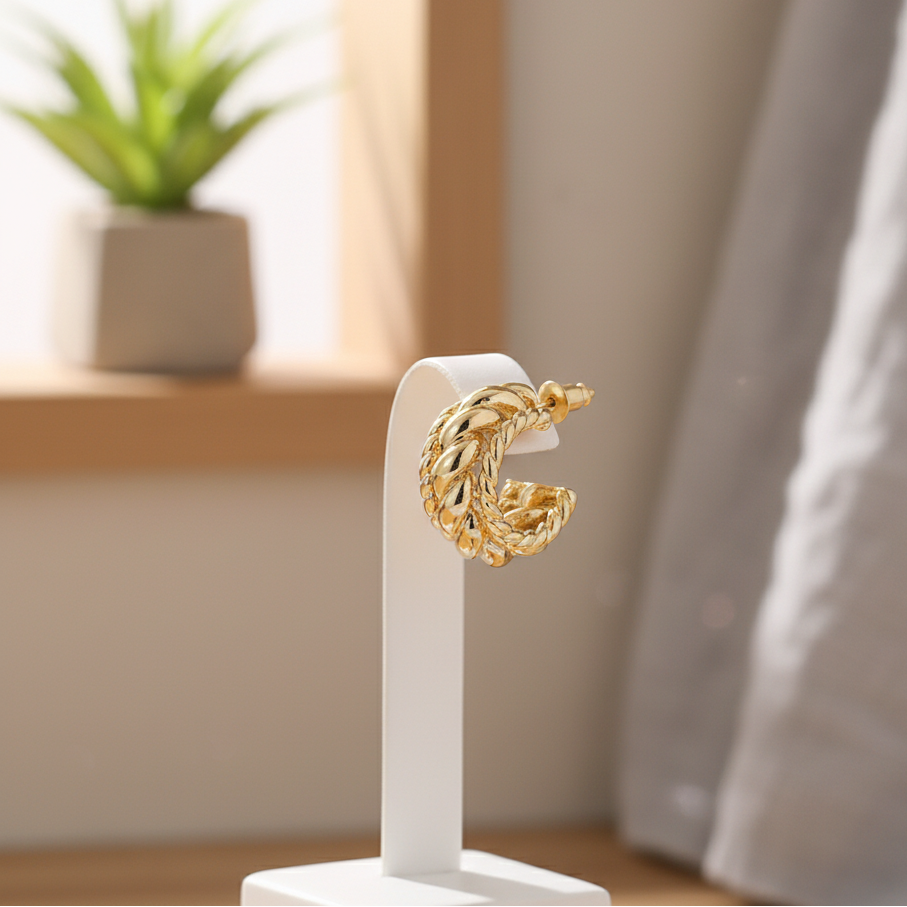 Dione Canada gold textured hoop earring displayed on a minimalist white stand in soft natural light, highlighting the intricate woven design.