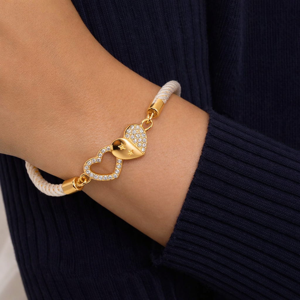 Gold bracelet with heart and diamond design on a wrist against a dark background