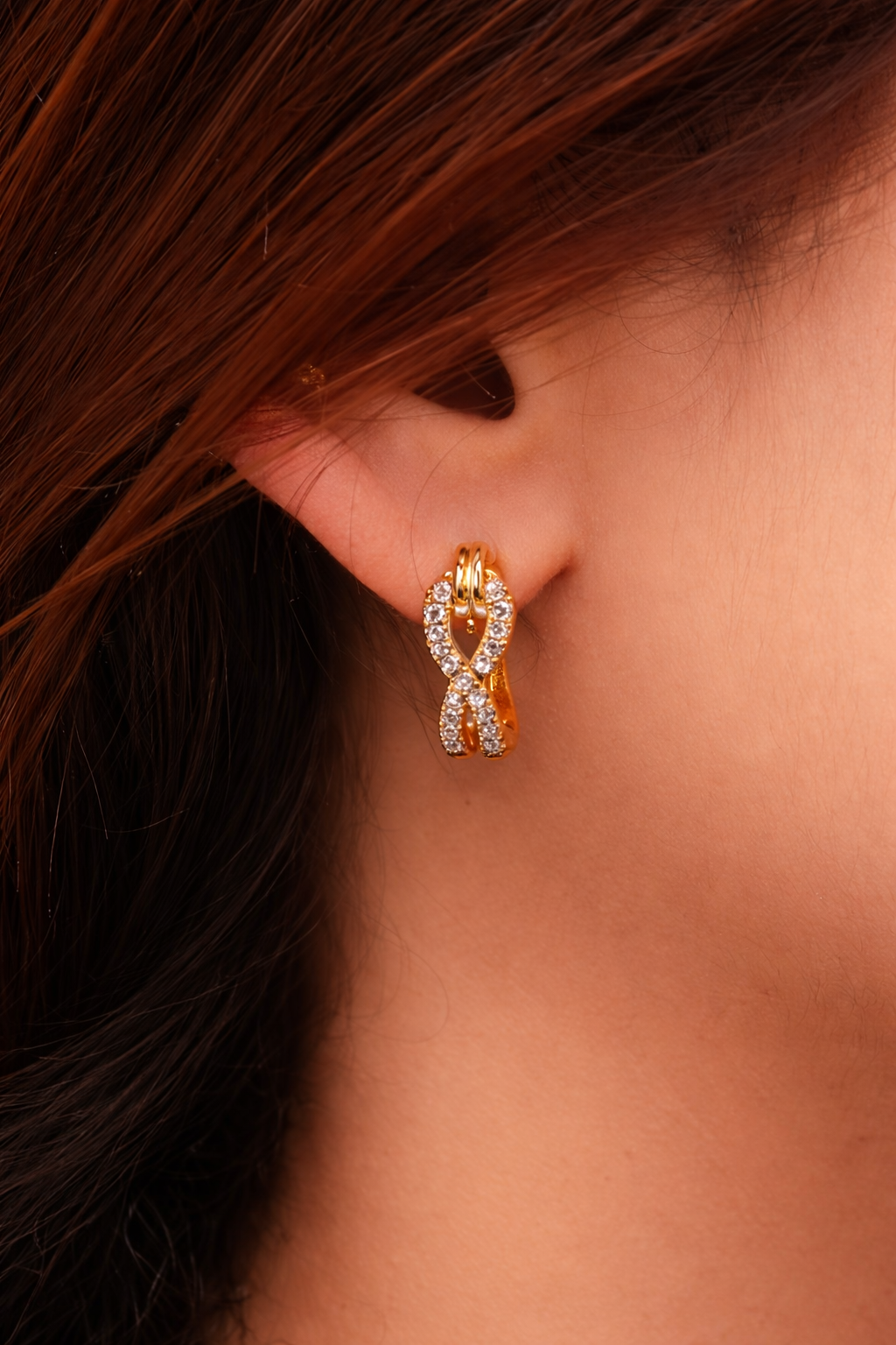 Gold infinity knot hoop earrings with diamond accents worn on ear, elegant minimalist jewelry for women