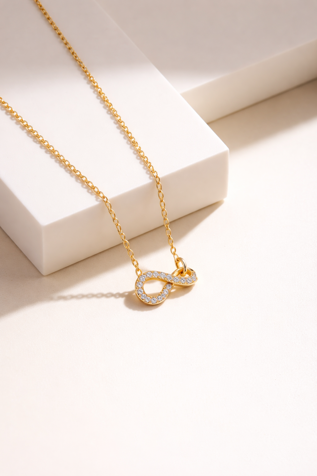 Gold infinity pendant necklace with diamond accents on neutral background, minimalist elegant jewelry