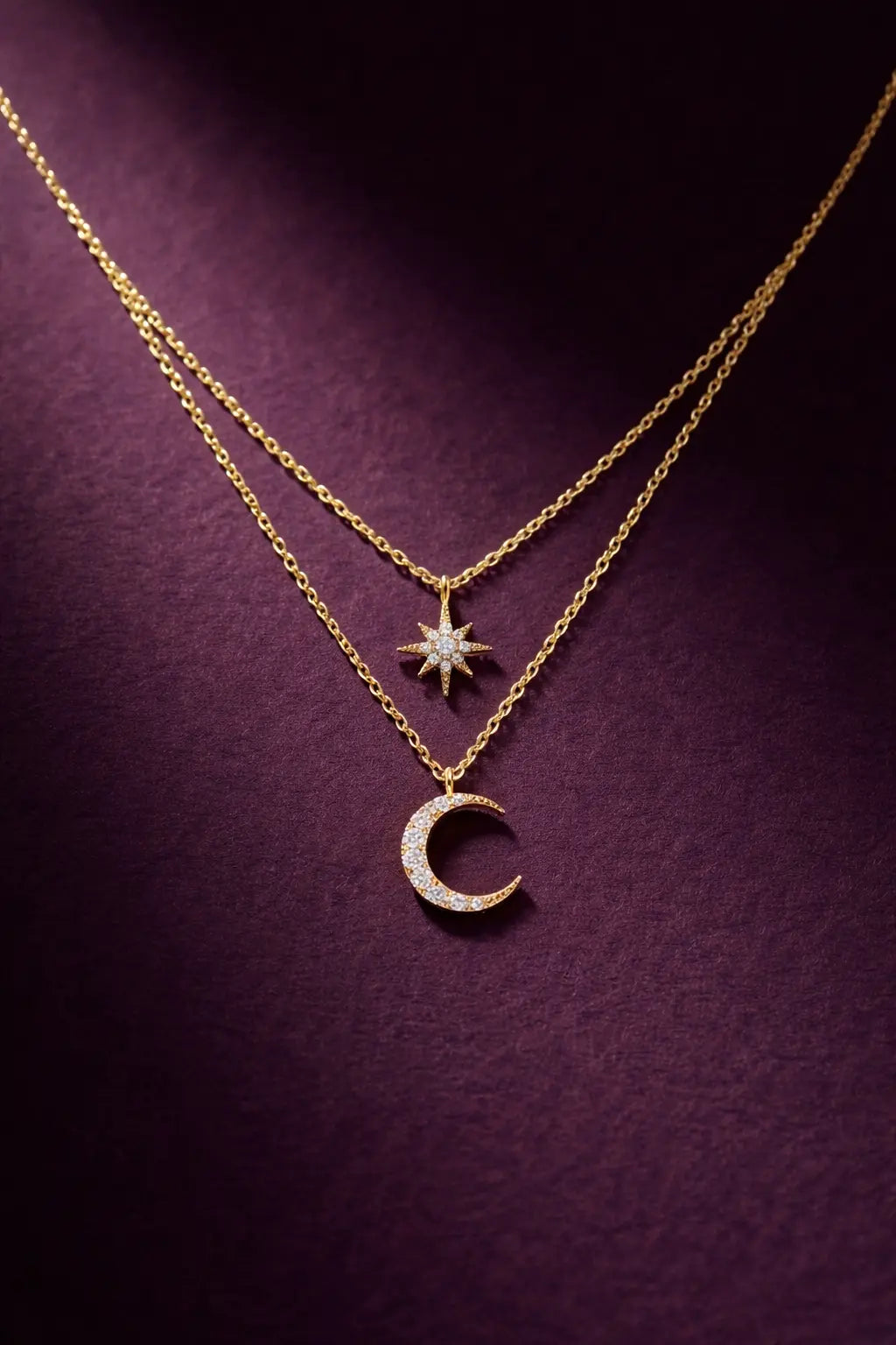 Two gold necklaces with star and moon pendants on a purple background