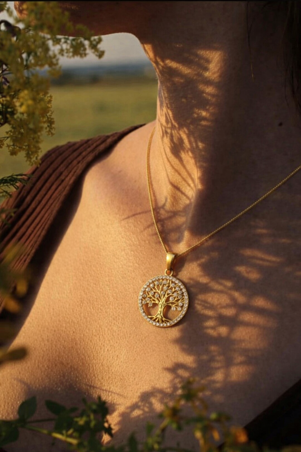 Gold necklace with a tree-of-life pendant worn by a person, with a blurred natural background.