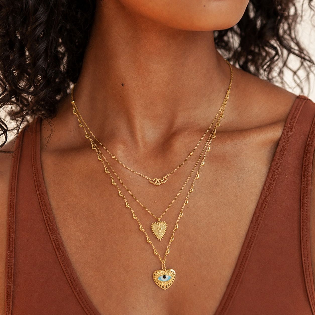 Woman wearing the Nazara Necklace, a layered gold evil eye heart necklace