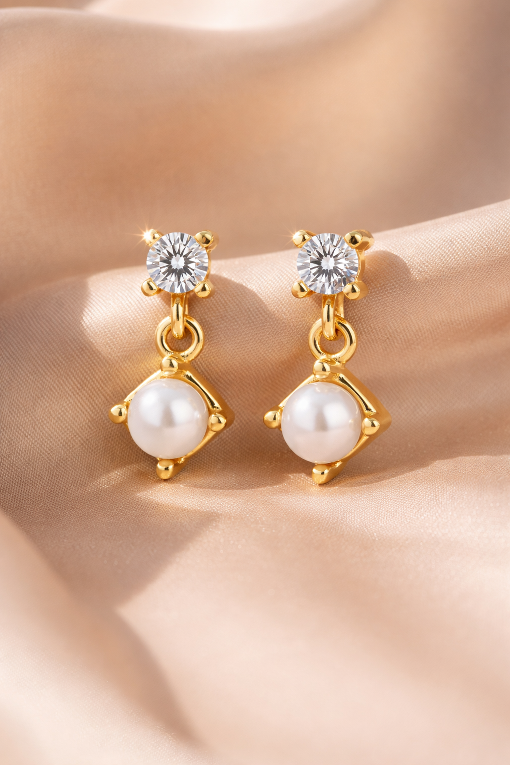 Gold earrings with pearls and clear stones on a soft fabric background