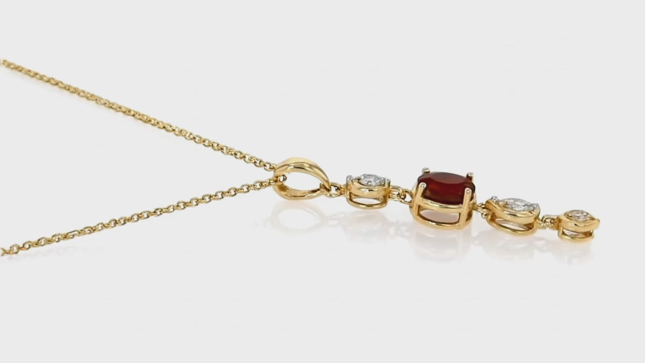 Gold drop necklace by Dione Canada featuring a deep red center gemstone with alternating crystal accents, luxury studio close-up.