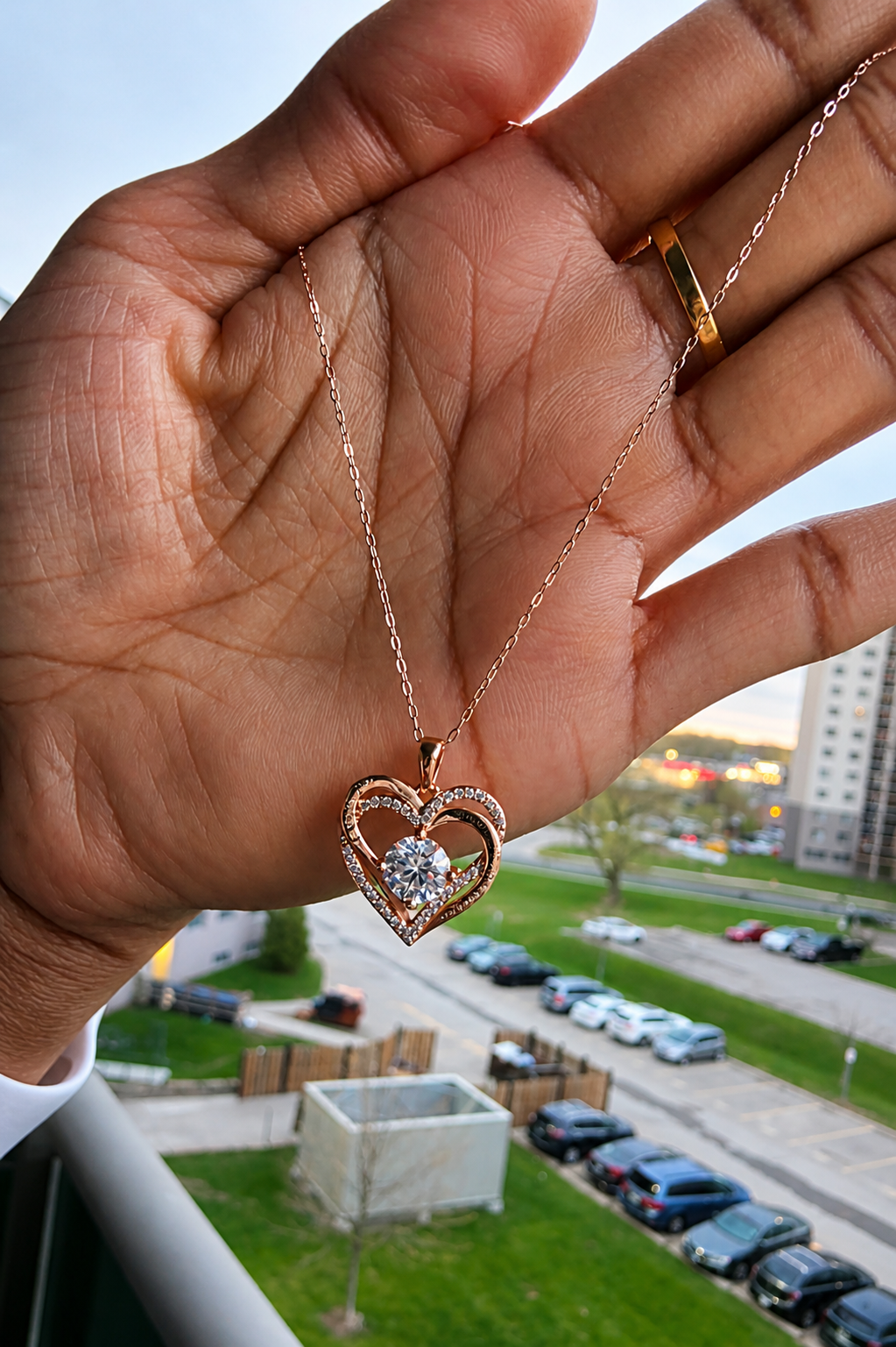 Heart-shaped necklace with a diamond pendant held in a hand, with a blurred outdoor background.