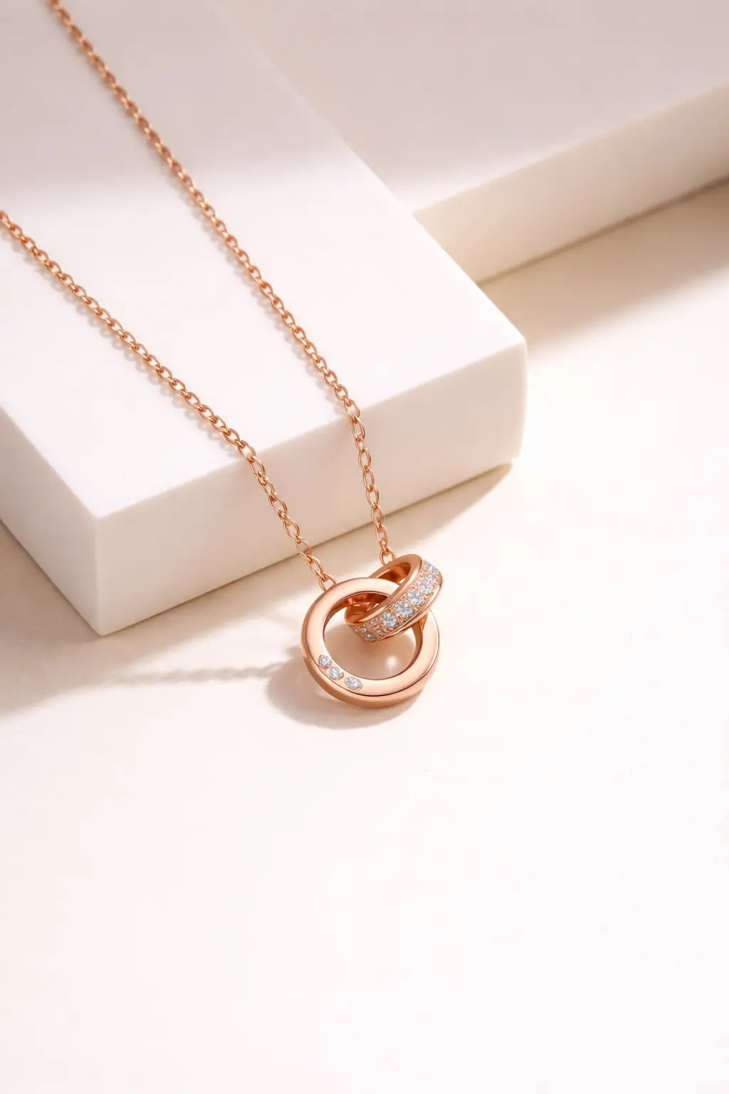 Rose gold interlocking circle pendant necklace with diamond accents on neutral background, elegant minimalist jewelry