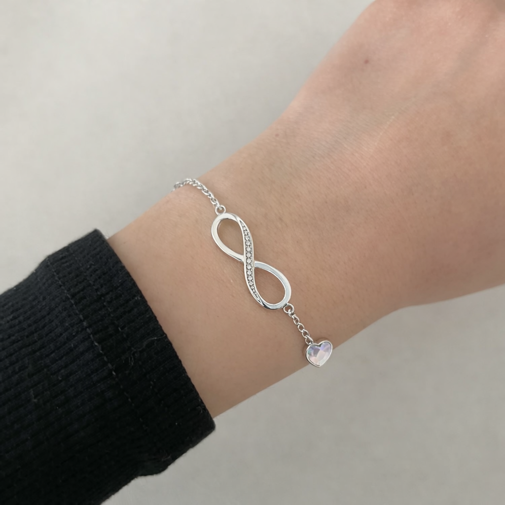Sterling silver infinity charm bracelet with small heart detail worn on wrist, minimalist elegant jewelry for women