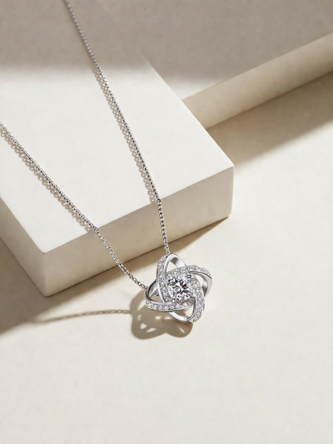 Sterling silver infinity knot pendant necklace with central diamond and accent stones on neutral background, elegant modern jewelry