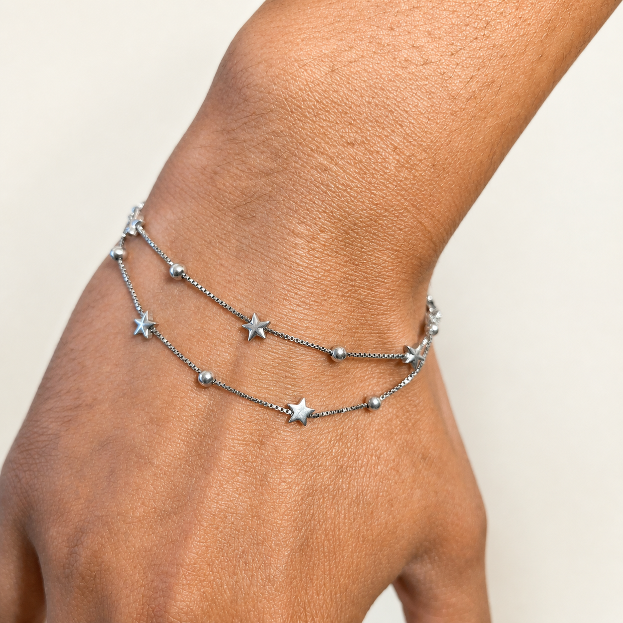 Silver anklets with star charms on a person's ankle against a neutral background